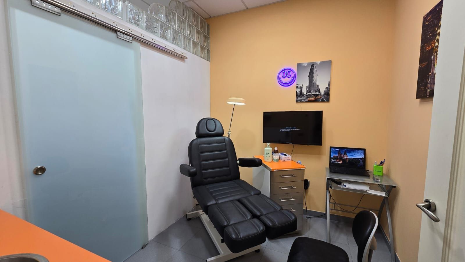 Sala de dentista y podología: silla negra, mesa pequeña paredes naranjas y puerta esmerilada.