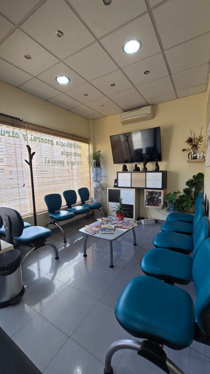 Sala de espera con sillas azules, televisión y mesa con revistas.