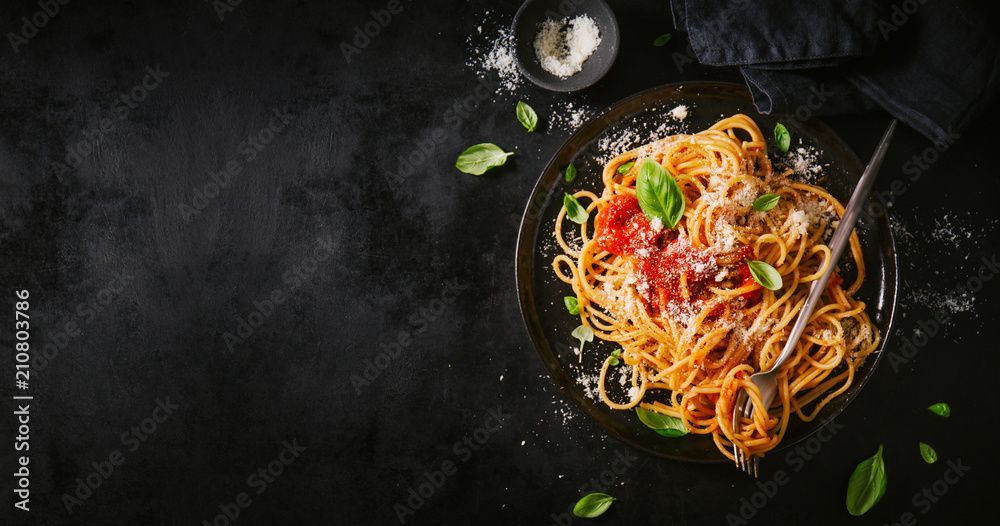Ein Teller Spaghetti mit Tomatensoße und Basilikum auf schwarzem Hintergrund.