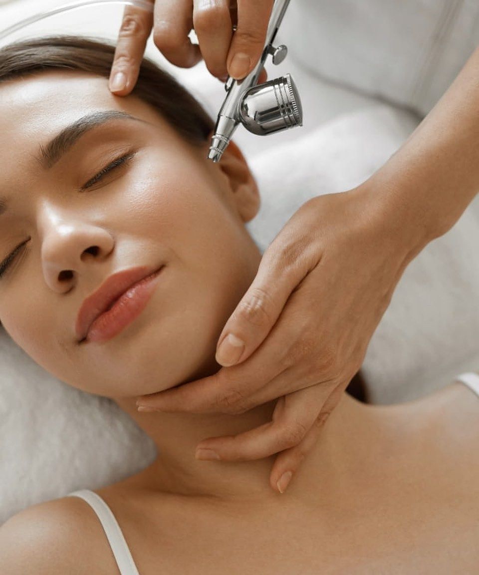 Tratamiento facial cosmético con un dispositivo de aerografía en la mejilla de una clienta relajada.