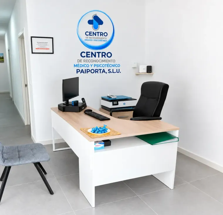 Mostrador de recepción de clínica con ordenador, silla negra y logotipo azul en la pared, en una oficina de color blanco