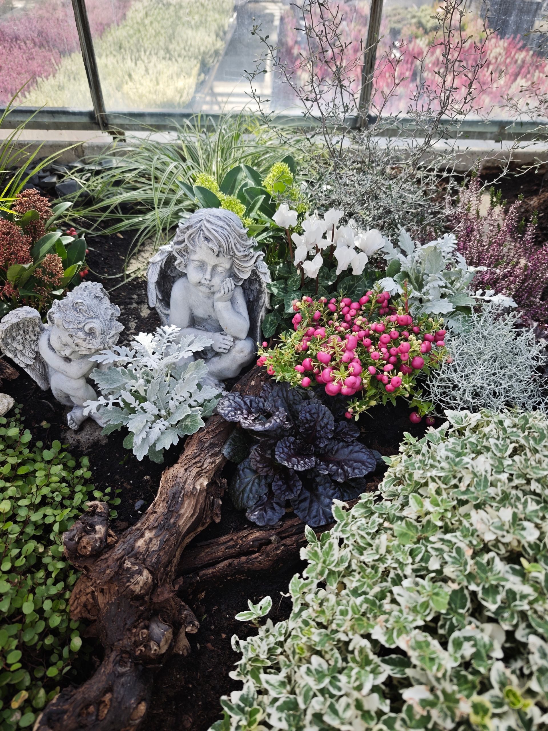 Kleiner Feengarten mit einem steinernen Engel, rosa Blüten und panaschiertem Laub in einem Pflanzkübel.