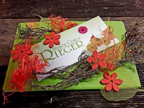 mit Zweigen und orangefarbenen Blumen verzierter grüner Gutschein von Blumen Center Rieger