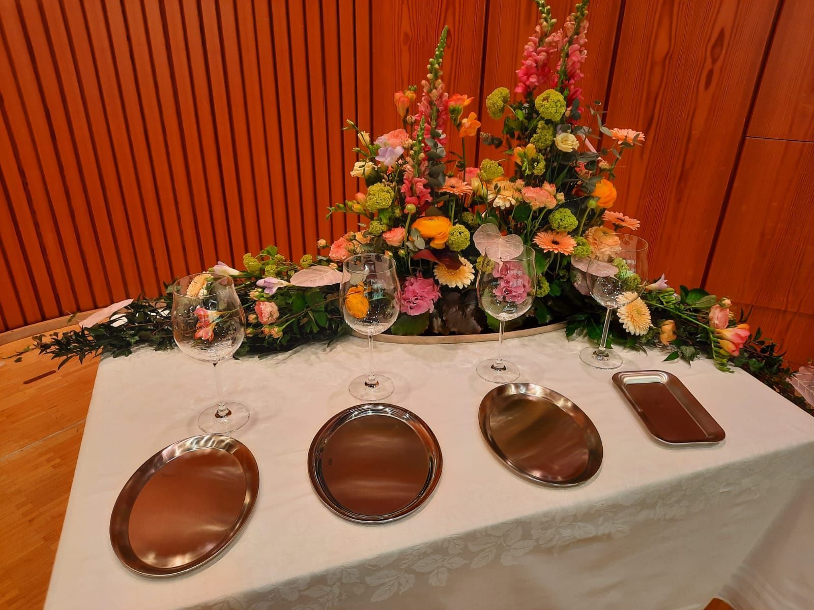 Festlich gedeckter Tisch mit Silbertellern und Weingläsern, mit Blumengesteck im Hintergrund