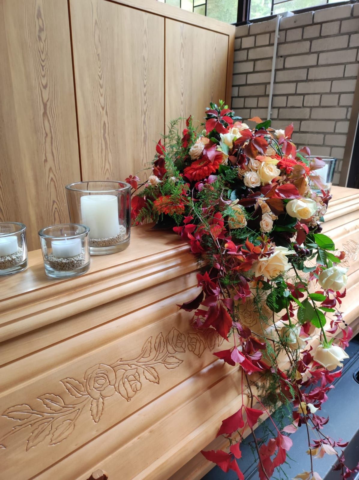 Blumengesteck auf einem Holzsarg in den Farben Weiß und Rot