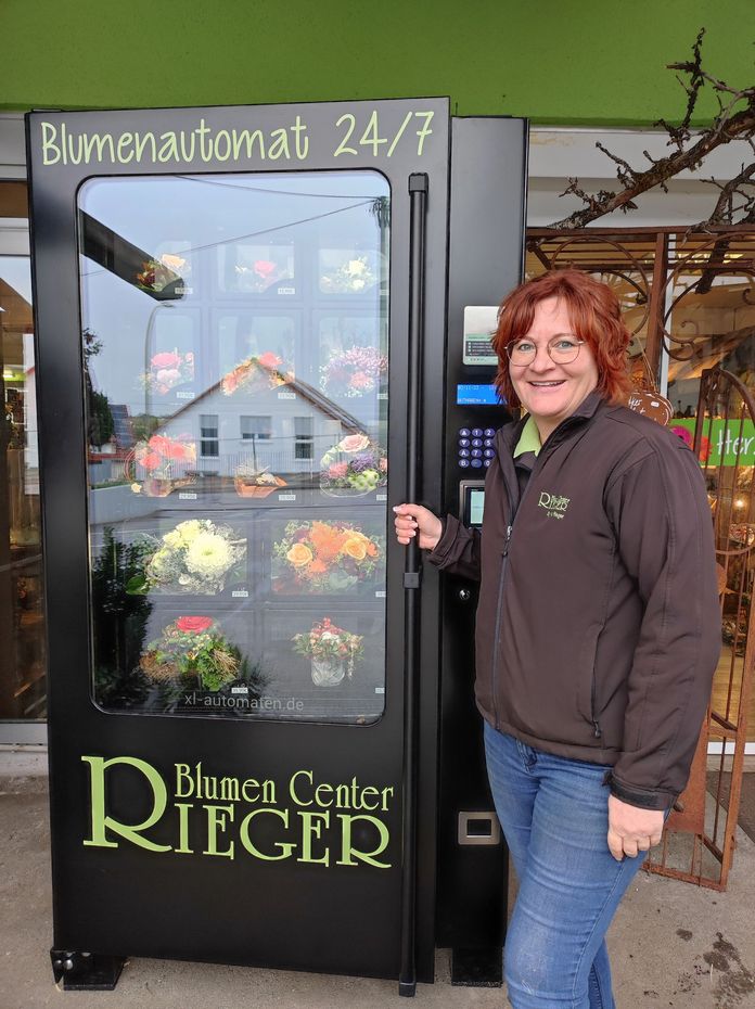 Mitarbeiterin vor einem Blumenautomaten mit frisch gebundenen Blumensträußen