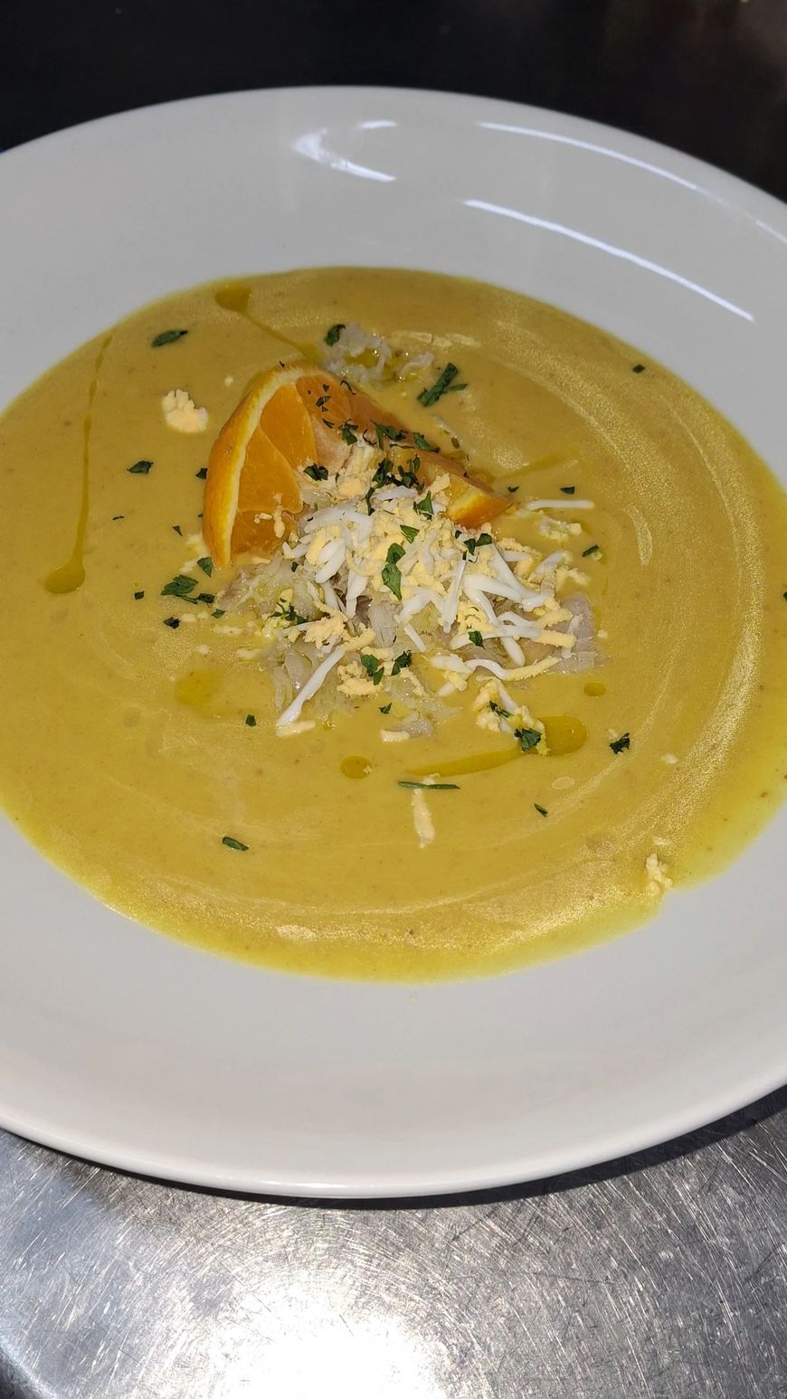 Un plato blanco cubierto con una sopa amarilla con queso y una rodaja de naranja.