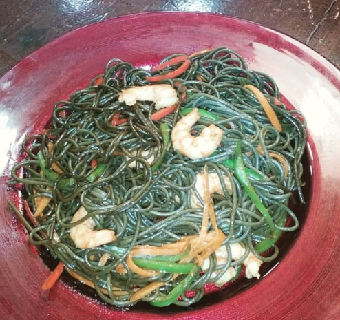Un tazón de fideos verdes con camarones y verduras
