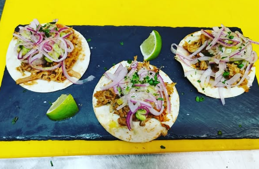 Tres tacos con cebollas y limas en una tabla de cortar