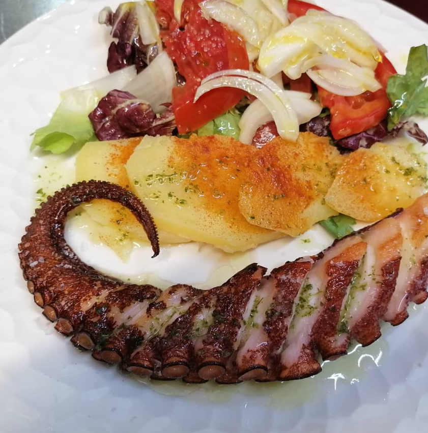 Un plato de comida con un pulpo y verduras encima.