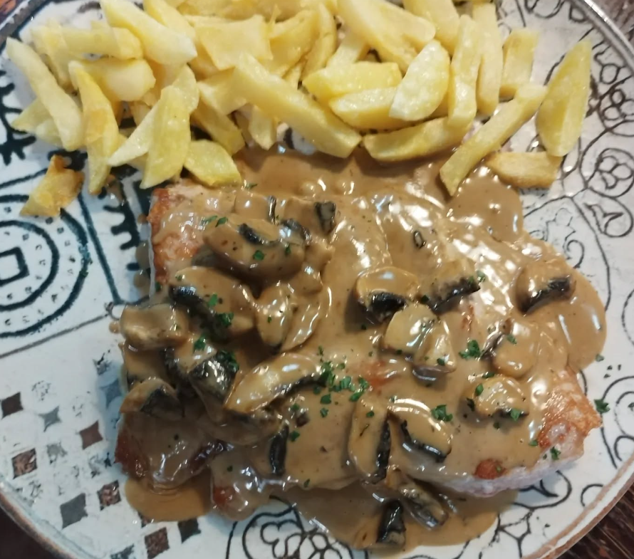 Un plato de comida con champiñones y patatas fritas en una mesa.