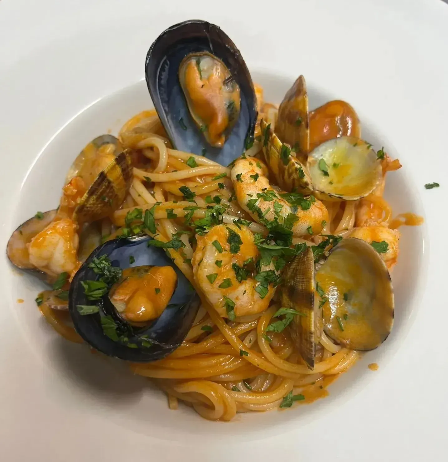Un plato blanco cubierto con espaguetis con almejas y camarones.