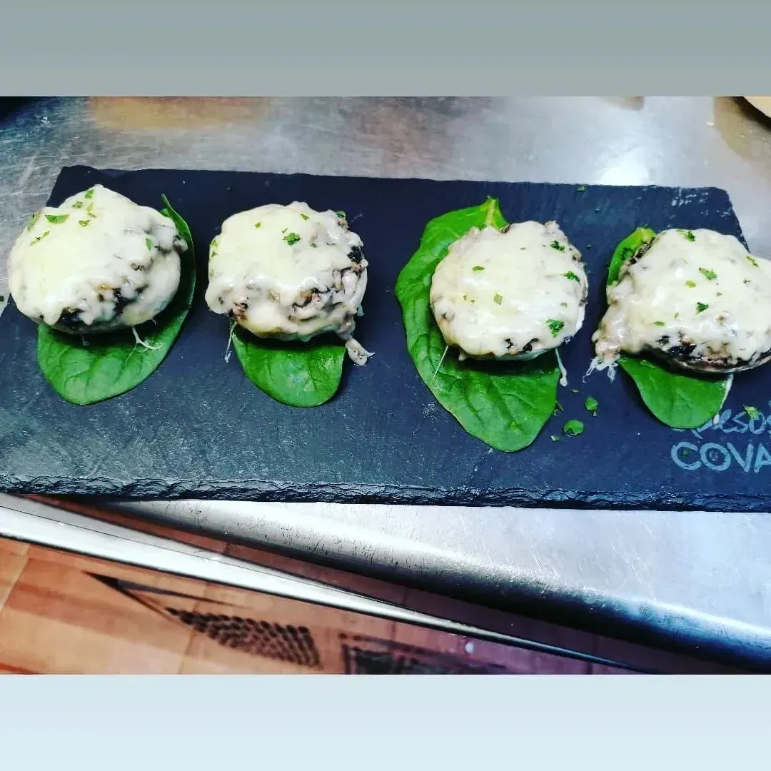 Cuatro piezas de comida en una bandeja de pizarra que dice cova.