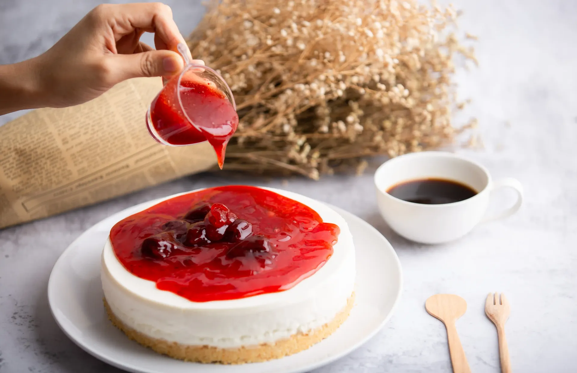 Una persona está vertiendo salsa de fresa sobre una tarta de queso.