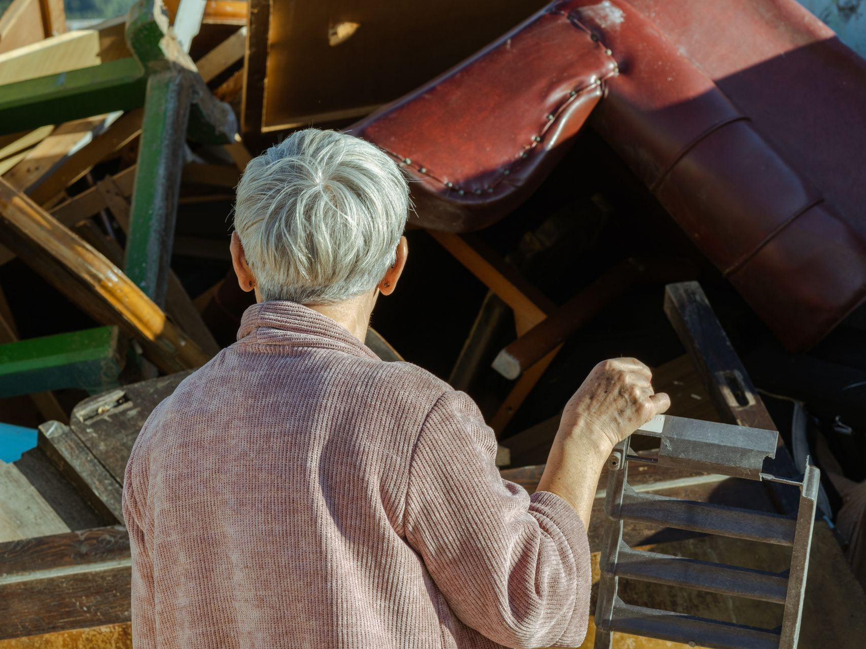 Une personne observe un tas de meubles mis au rebut ; une chaise rouge est visible.