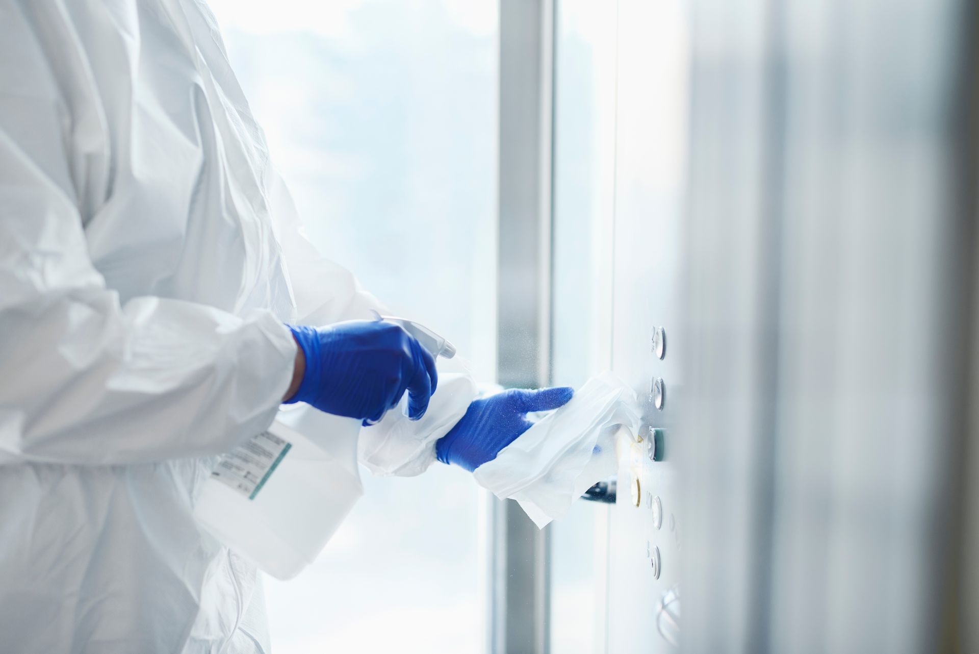 Une personne en combinaison de protection désinfecte une poignée de porte.