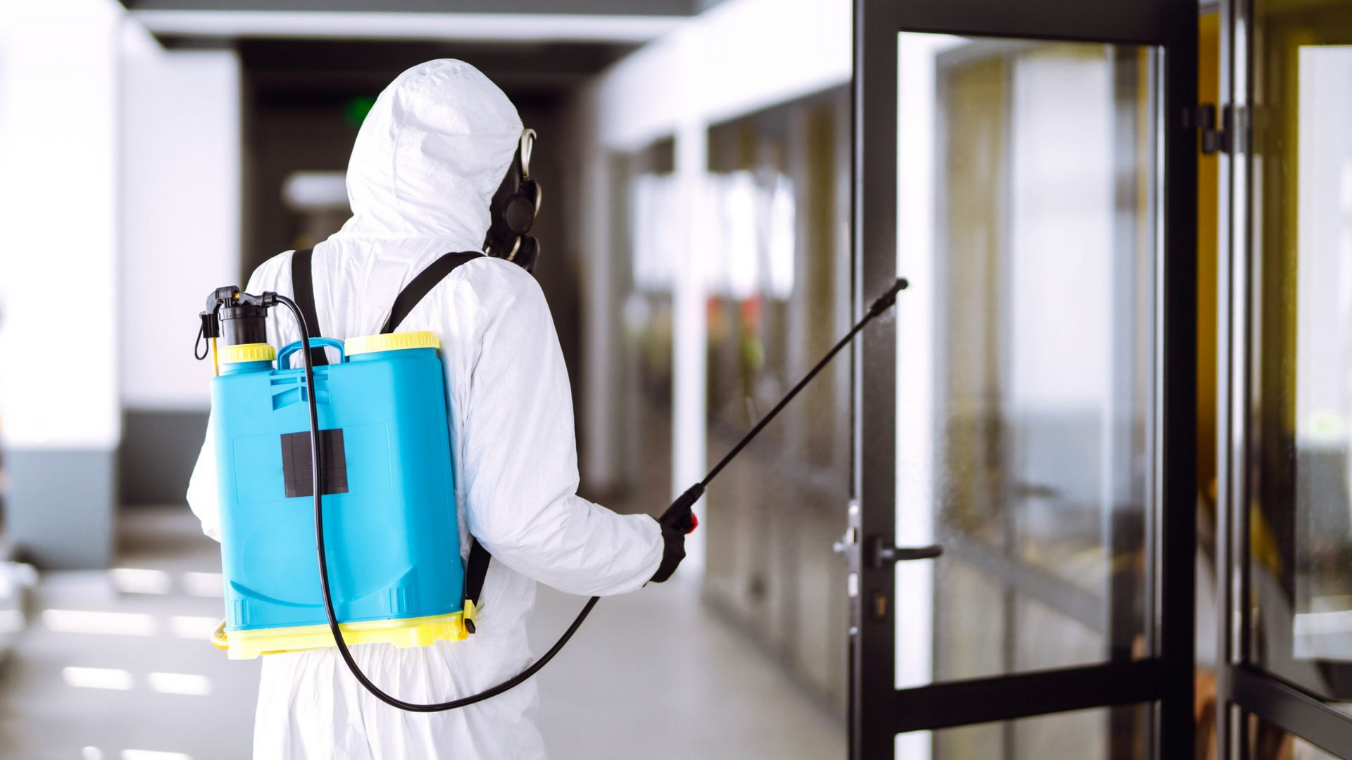 Une personne en combinaison de protection pulvérise du désinfectant dans un couloir.