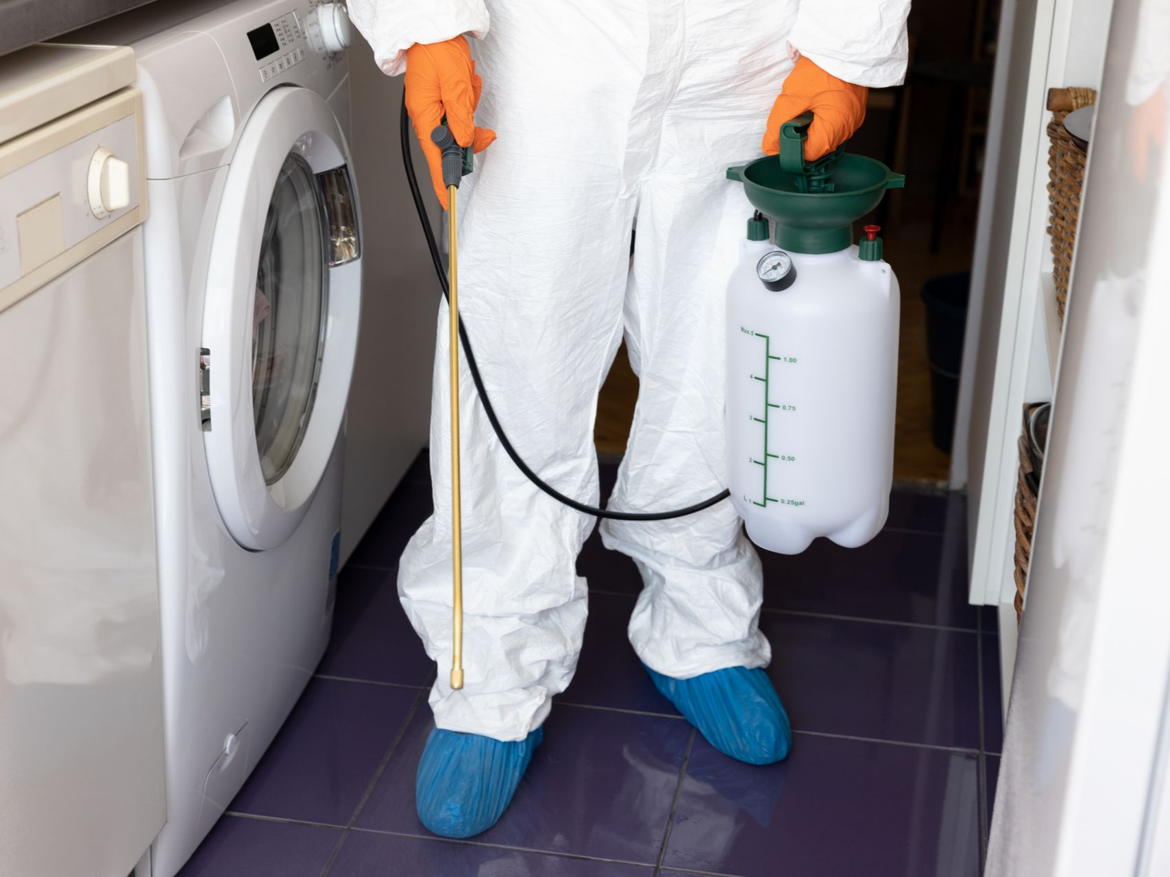 Une personne en combinaison de protection pulvérise de l'insecticide près d'une machine à laver.