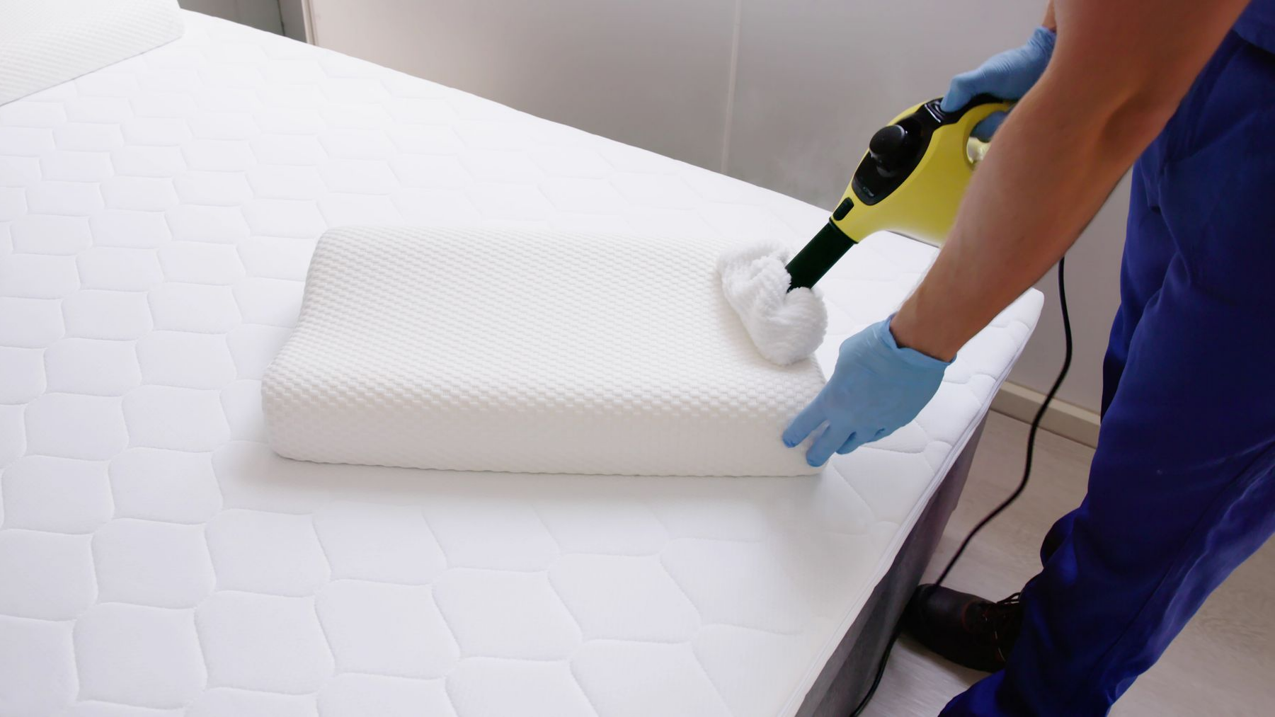 Une personne nettoie à la vapeur un oreiller blanc sur un matelas.