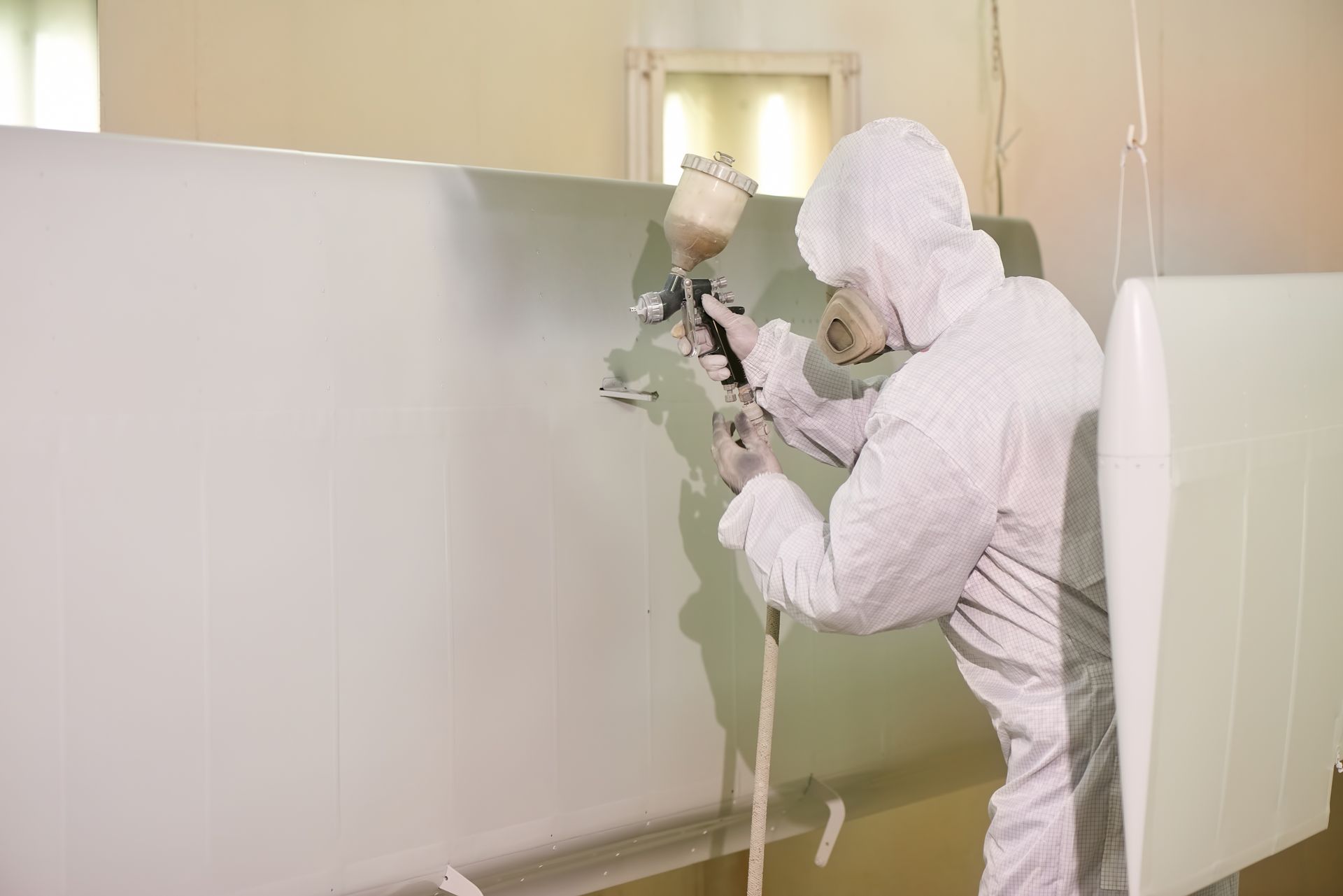 Ein Mann im Schutzanzug besprüht einen Flugzeugteil mit Farbe.