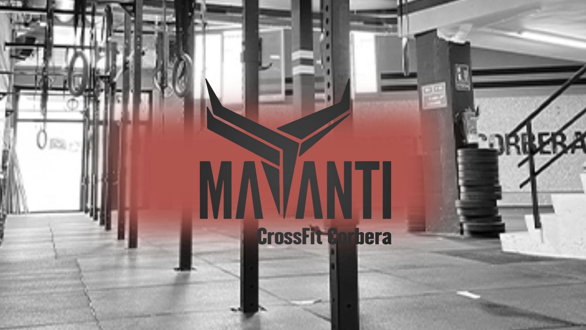 Logotipo de gimnasio rojo y negro con la inscripción “MAMANTI CrossFit” sobre un fondo interior de gimnasio.