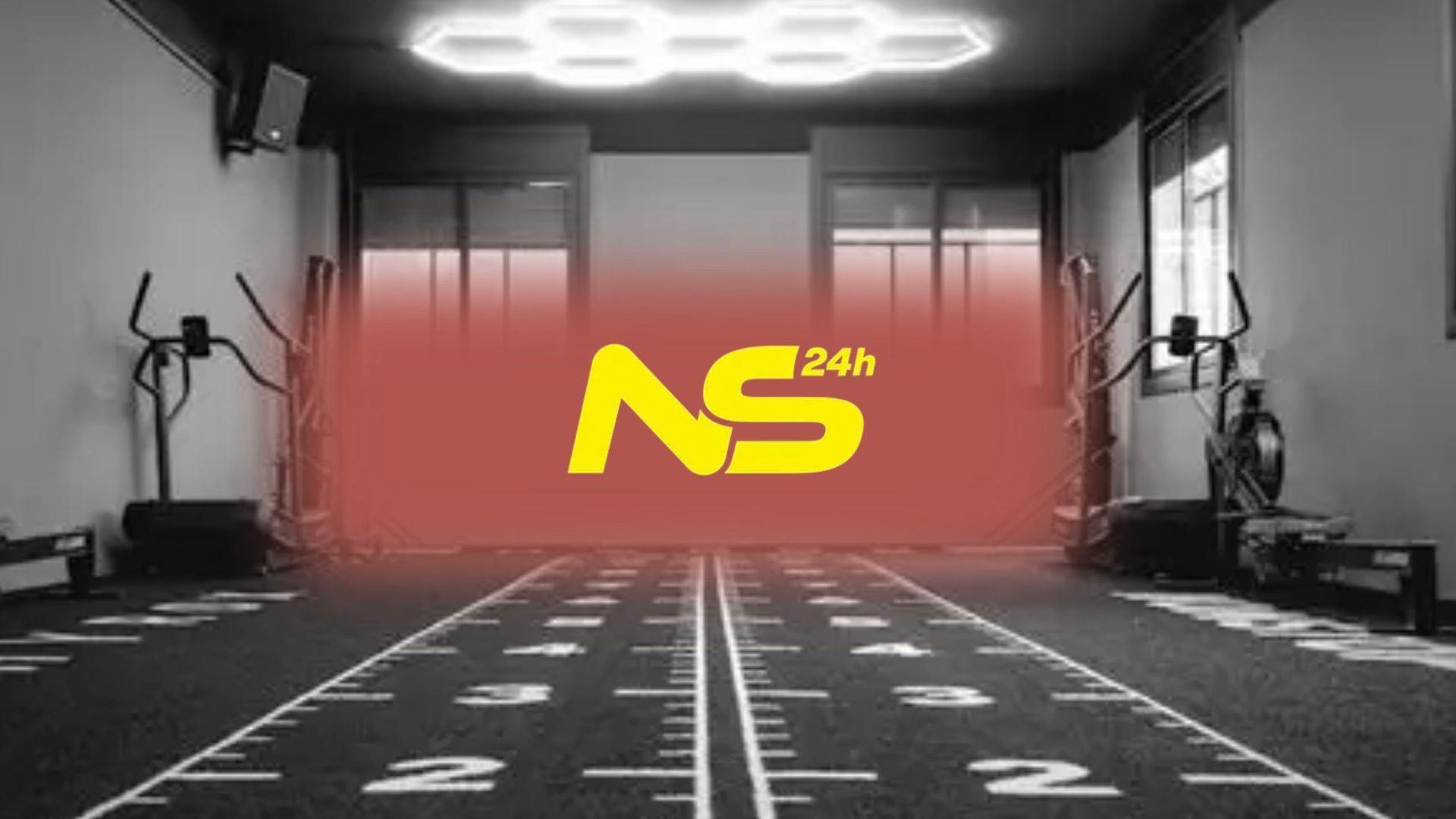 Interior de gimnasio con un logotipo central rojo brillante sobre un suelo de pista negro y equipos de fitness a ambos lados.