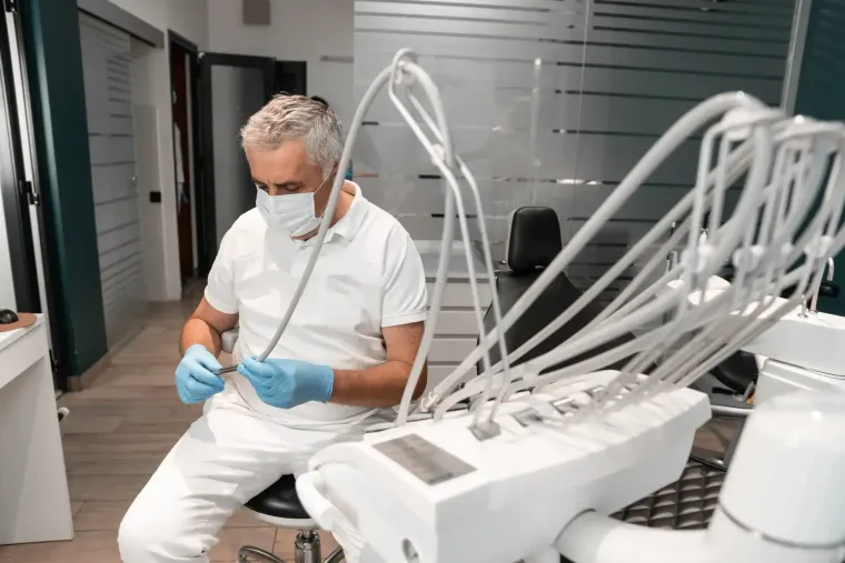 Técnico con uniforme blanco y mascarilla examinando un dispositivo de laboratorio con múltiples tubos en un entorno clínico.