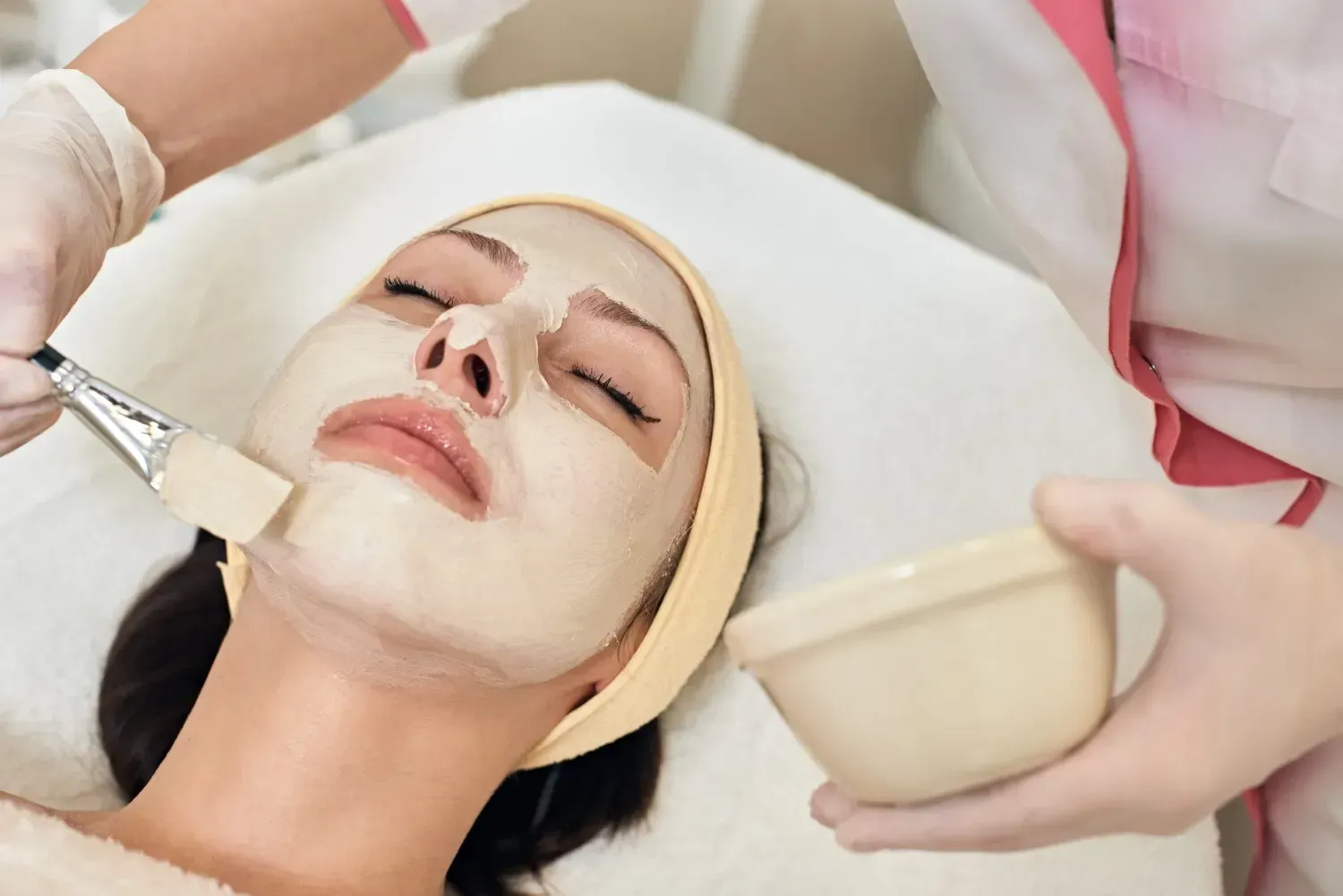 Tratamiento de belleza que consiste en la aplicación de una mascarilla facial con brocha a una persona reclinada en un entorno de spa.