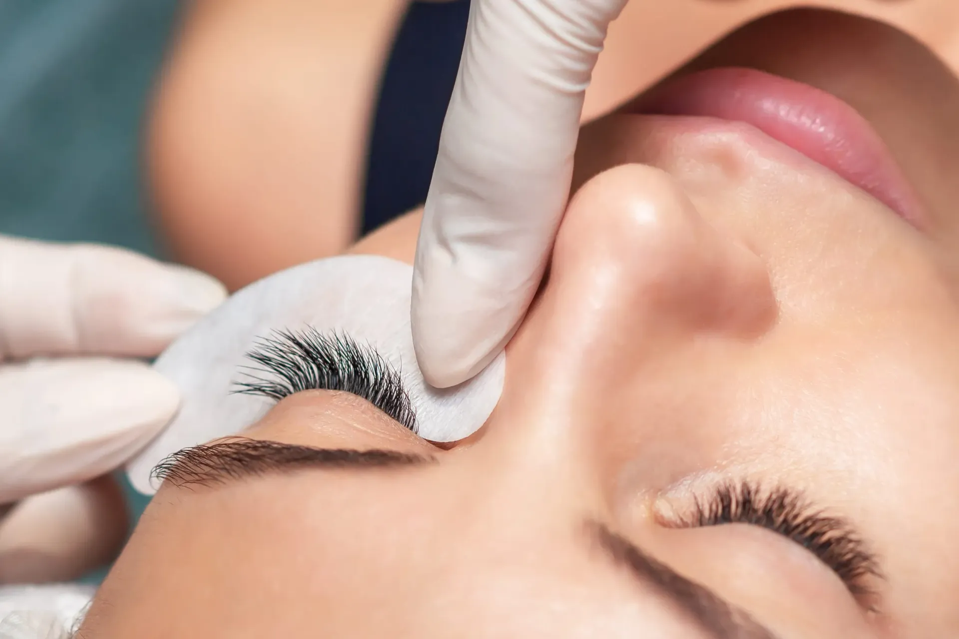 Manos enguantadas aplicando un tratamiento de pestañas en el ojo cerrado de una mujer en un entorno de spa.