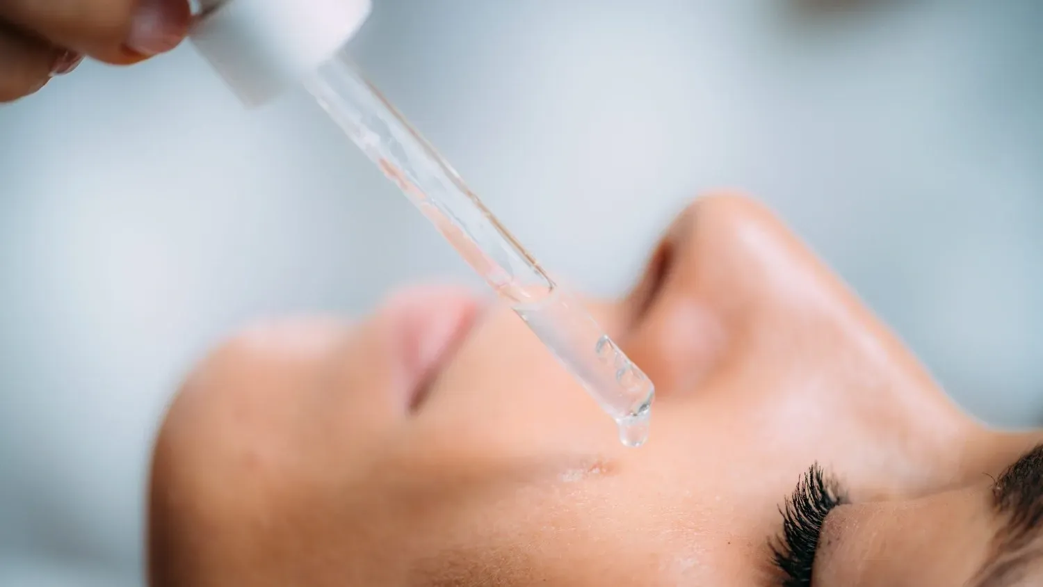 Primer plano de una persona recibiendo un suero facial con un gotero cerca de la nariz.