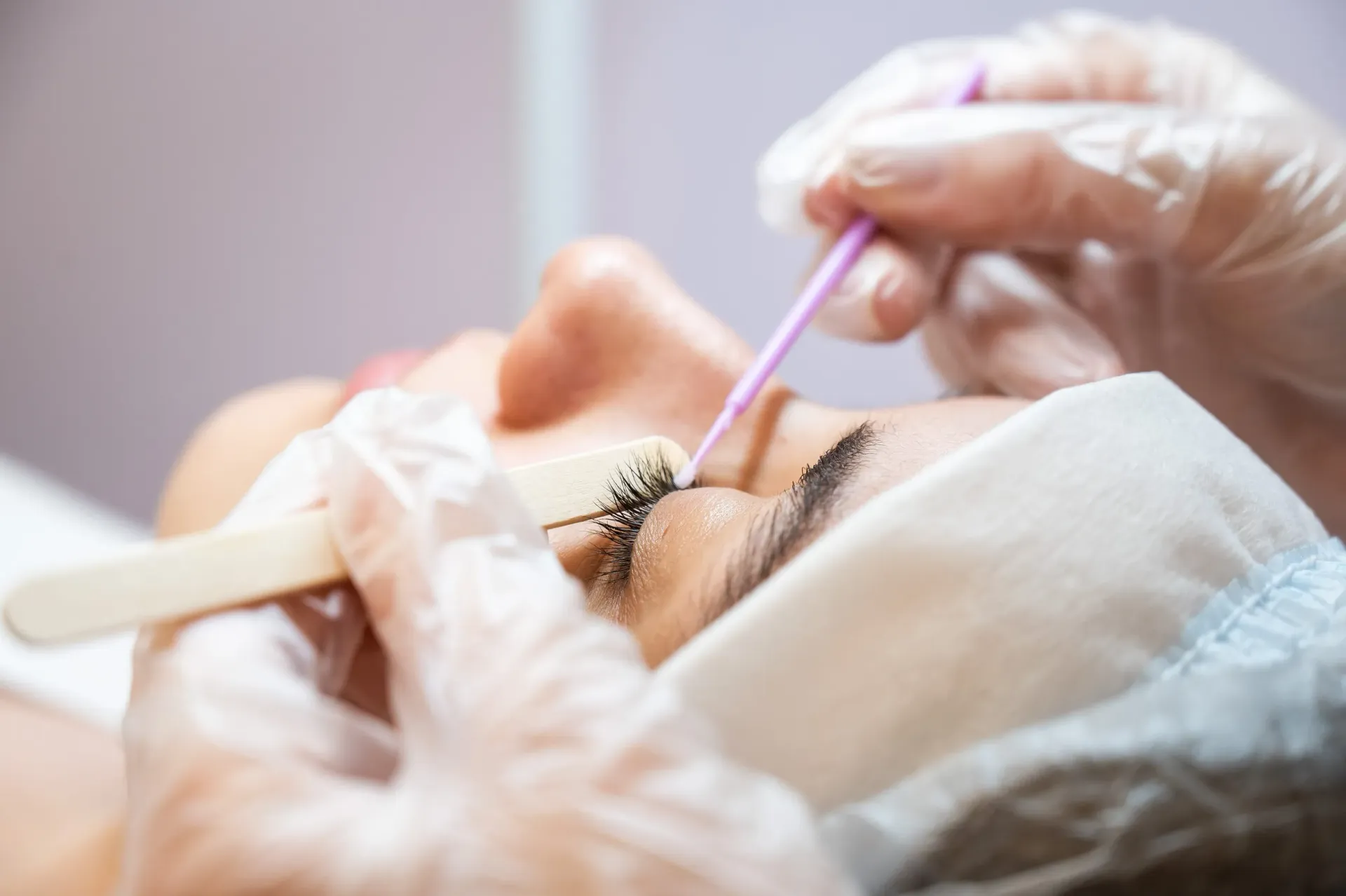 Técnica aplicando extensiones de pestañas a una clienta con los ojos cerrados durante un tratamiento de belleza.