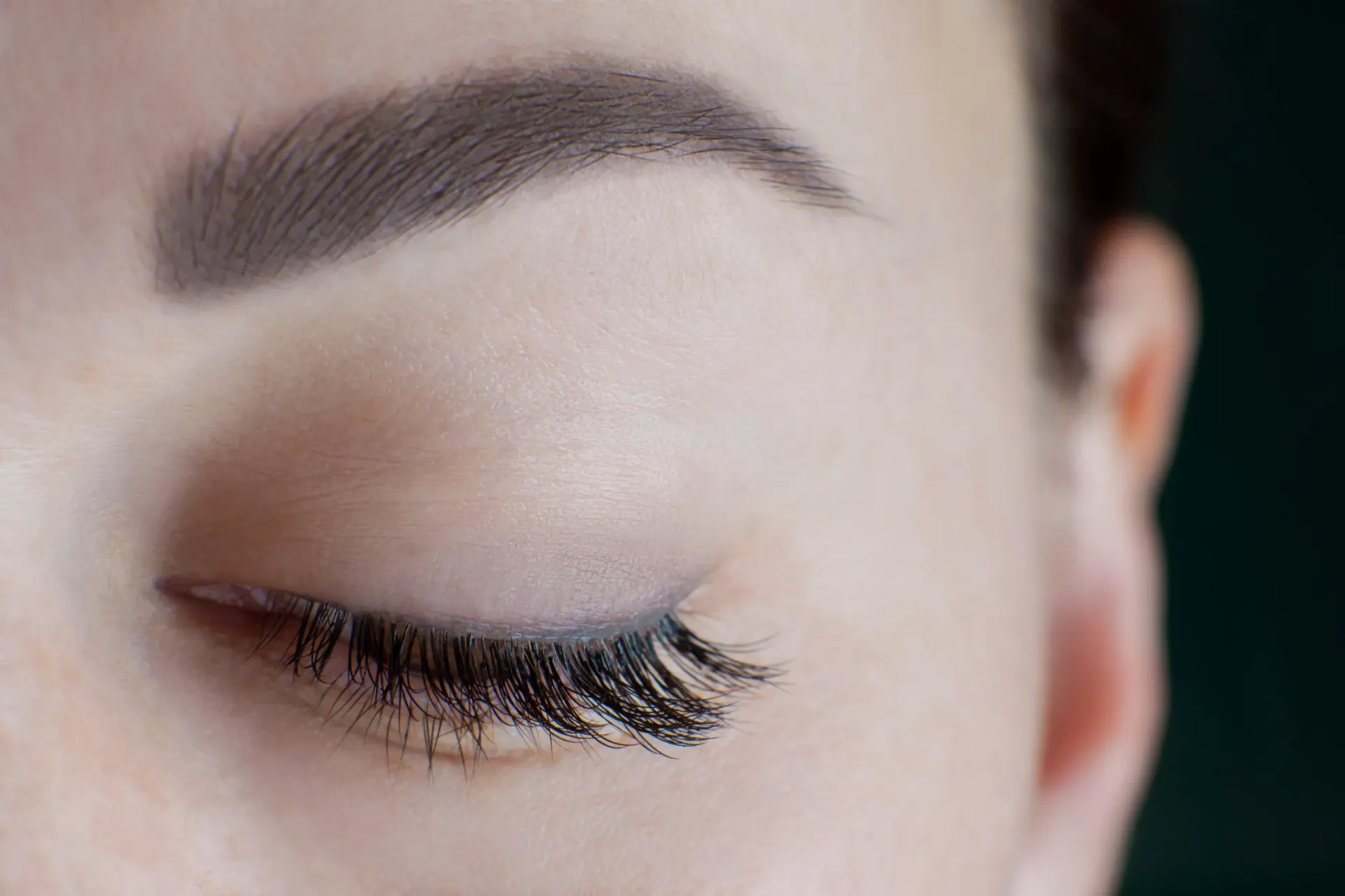 Primer plano de un ojo cerrado con maquillaje oscuro y una ceja perfilada.