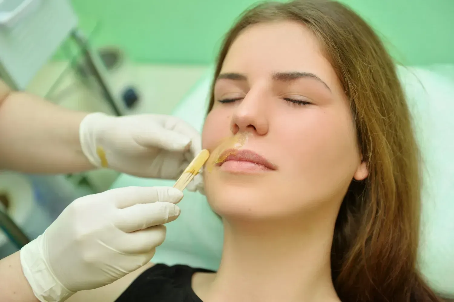 En una clínica, un profesional sanitario con guantes inyecta relleno en los labios de una mujer, que permanece sentada con los ojos cerrados.