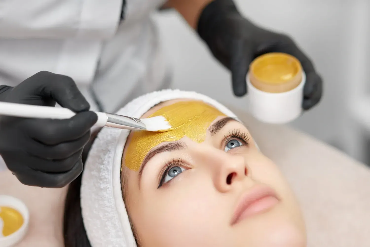 Tratamiento cosmético con mascarilla facial amarilla aplicada con manos enguantadas