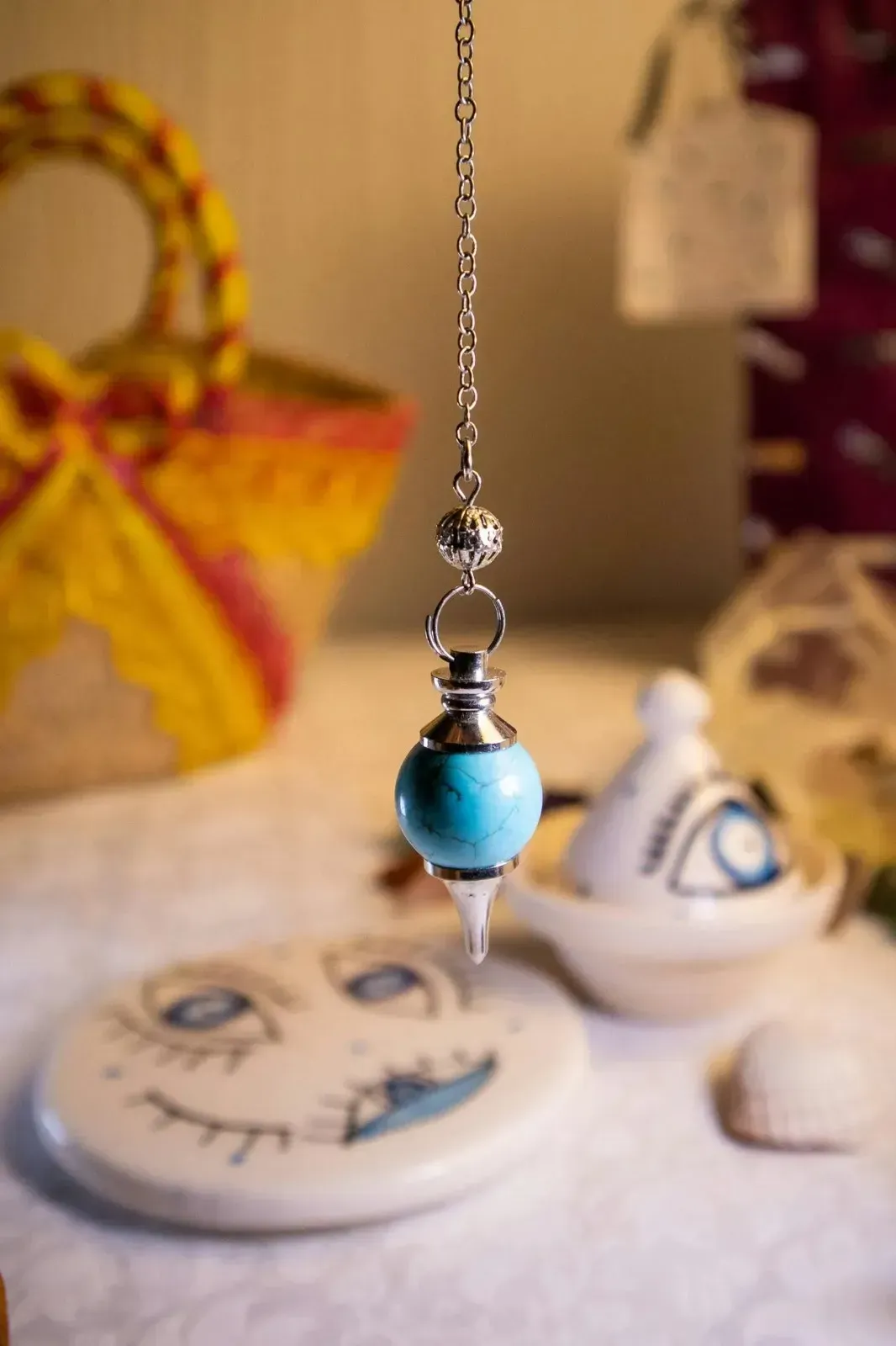 Colgante de cuentas azules que cuelga sobre un plato de cerámica blanca en una mesa con cerámica decorativa al fondo.