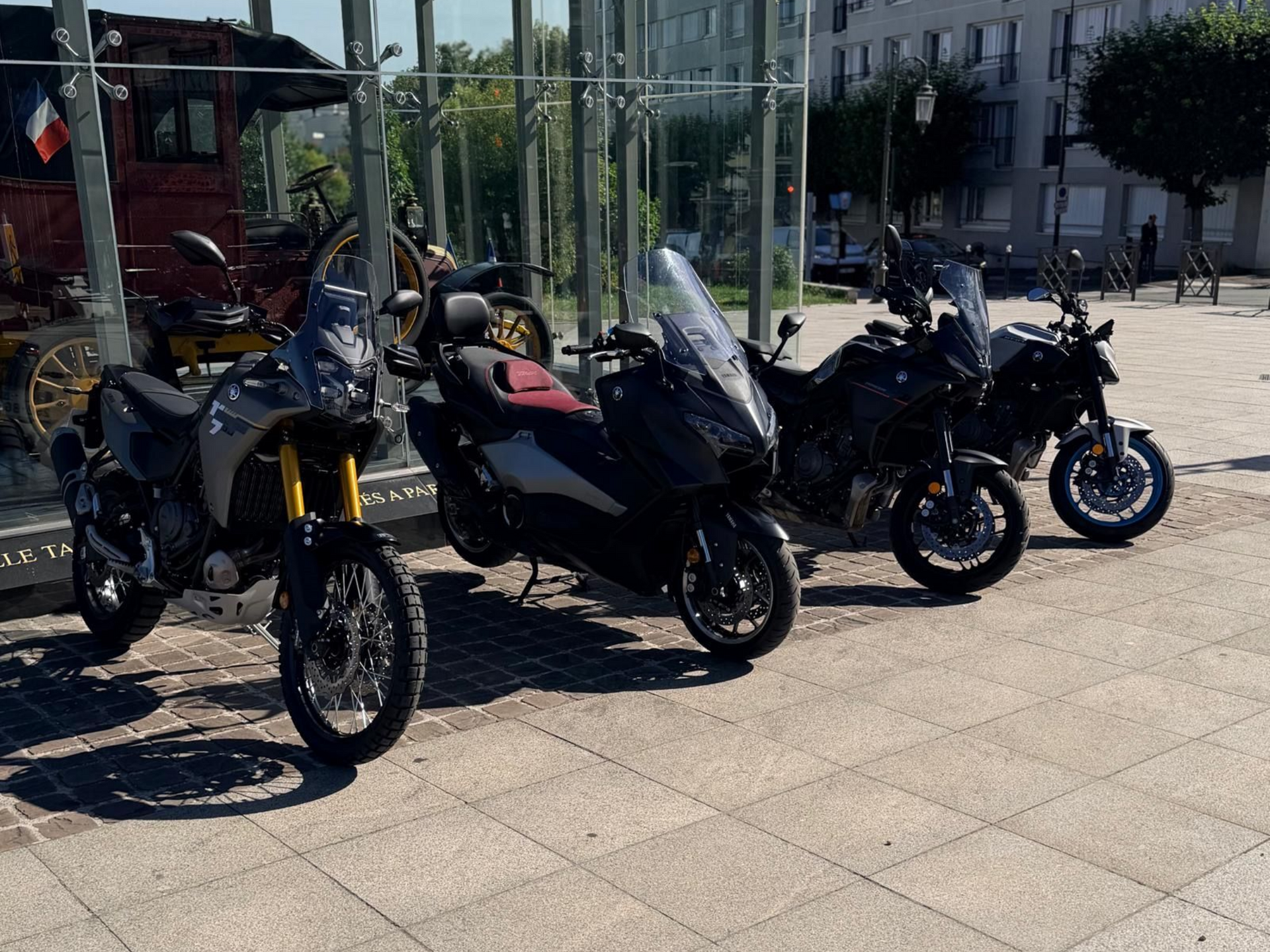 Deux motos noires garées dans un garage sombre, l'une avec des roues bleu vif et l'autre avec des touches de rouge.
