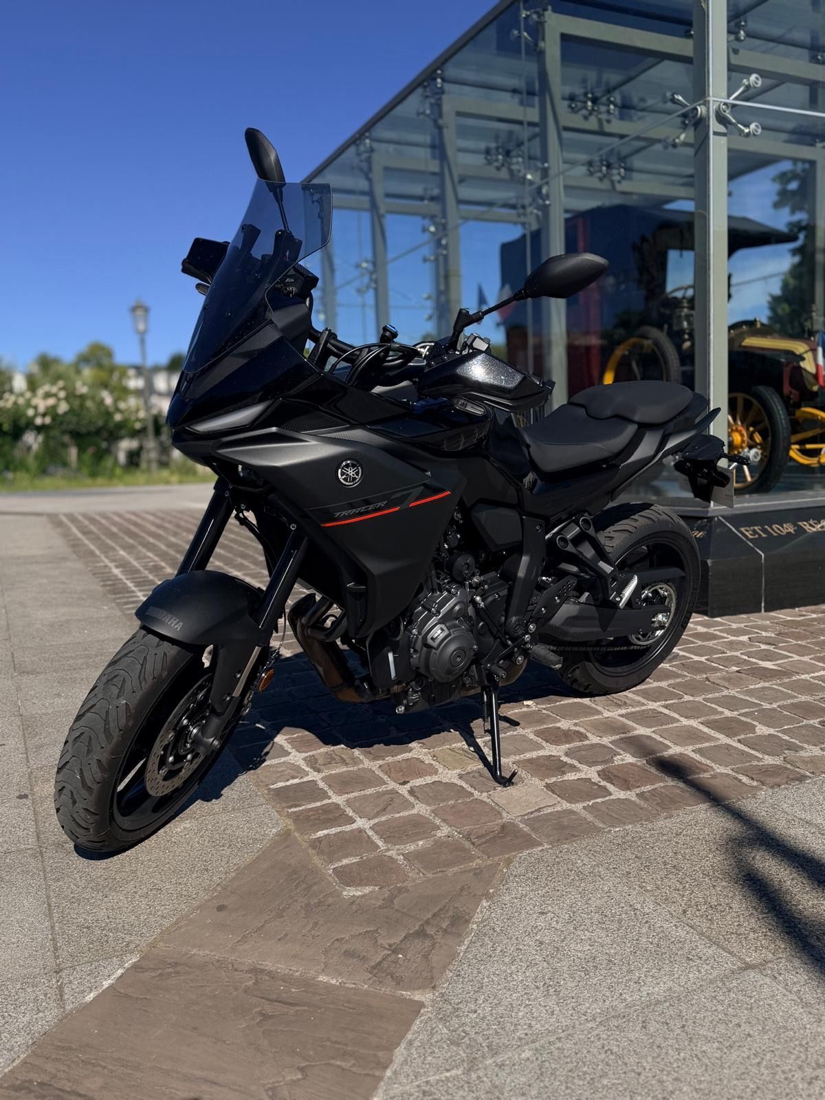 Deux motos noires garées côte à côte sur un trottoir mouillé, près d'un mur de briques.