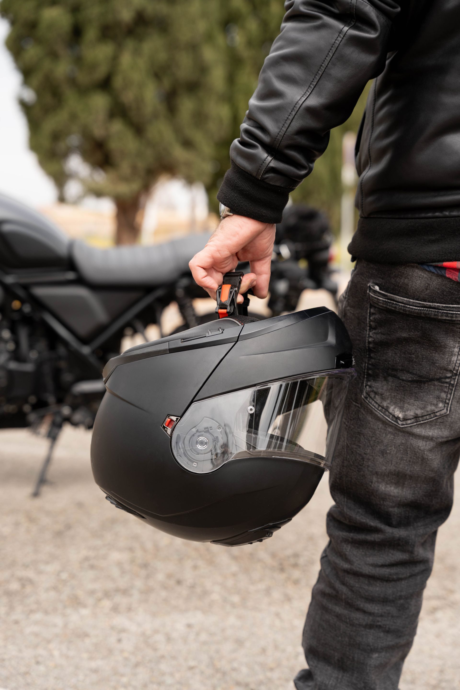 Une personne portant un casque de moto noir à l'extérieur, avec des motos garées en arrière-plan.