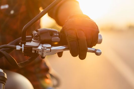 Main gantée agrippant le guidon d'une moto dans la douce lumière du coucher de soleil