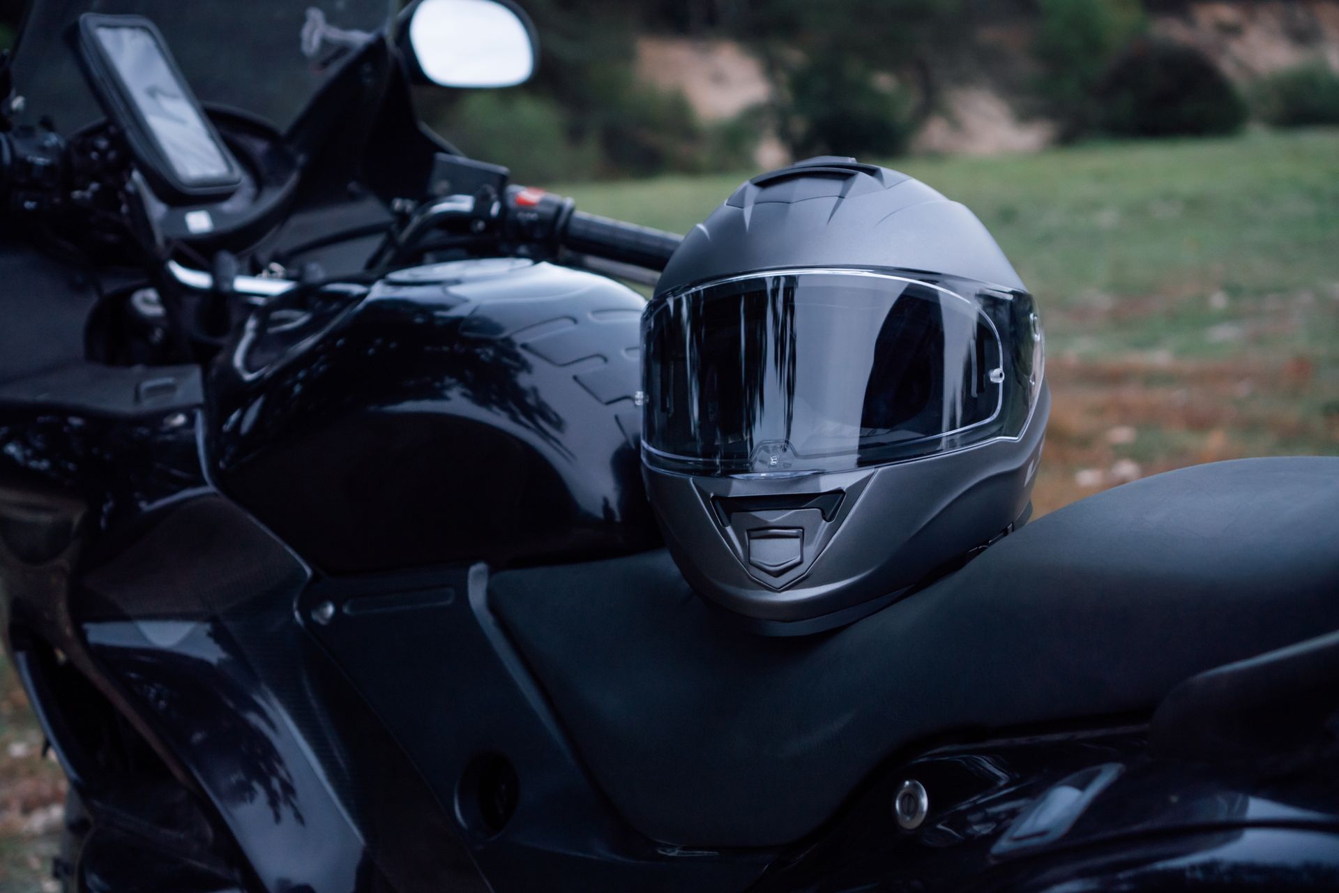 Moto noire avec un casque intégral réfléchissant sur la selle, garée à l'extérieur.
