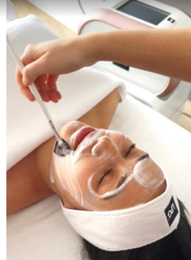 Des pieds vernis en noir, effleurés par une main tenant une fleur, probablement dans un salon de beauté.
