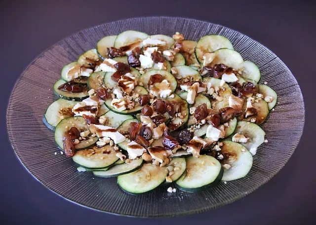 Un plato de vidrio cubierto con rodajas de calabacín y nueces.