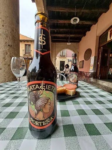 Una botella de cerveza reposa sobre un mantel a cuadros.