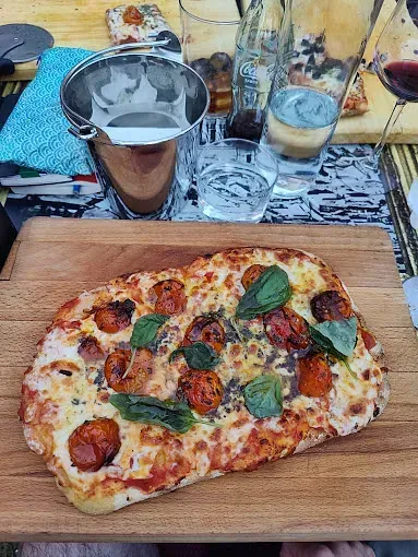 Una pizza está colocada sobre una tabla de cortar de madera sobre una mesa.