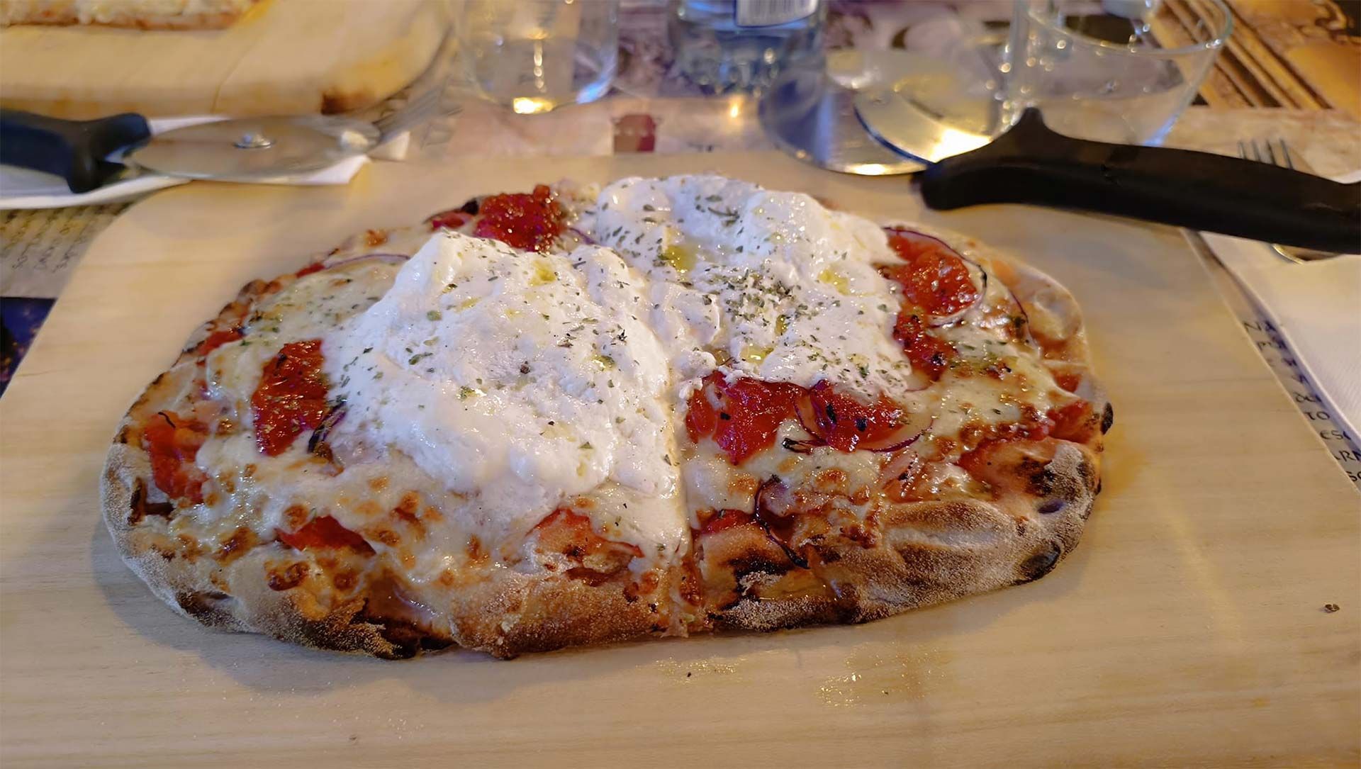Una pizza con tomates y queso está sobre una tabla de cortar de madera.