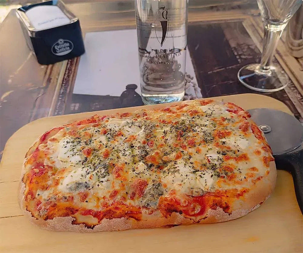 Una pizza sobre una tabla de cortar de madera junto a un vaso de agua.