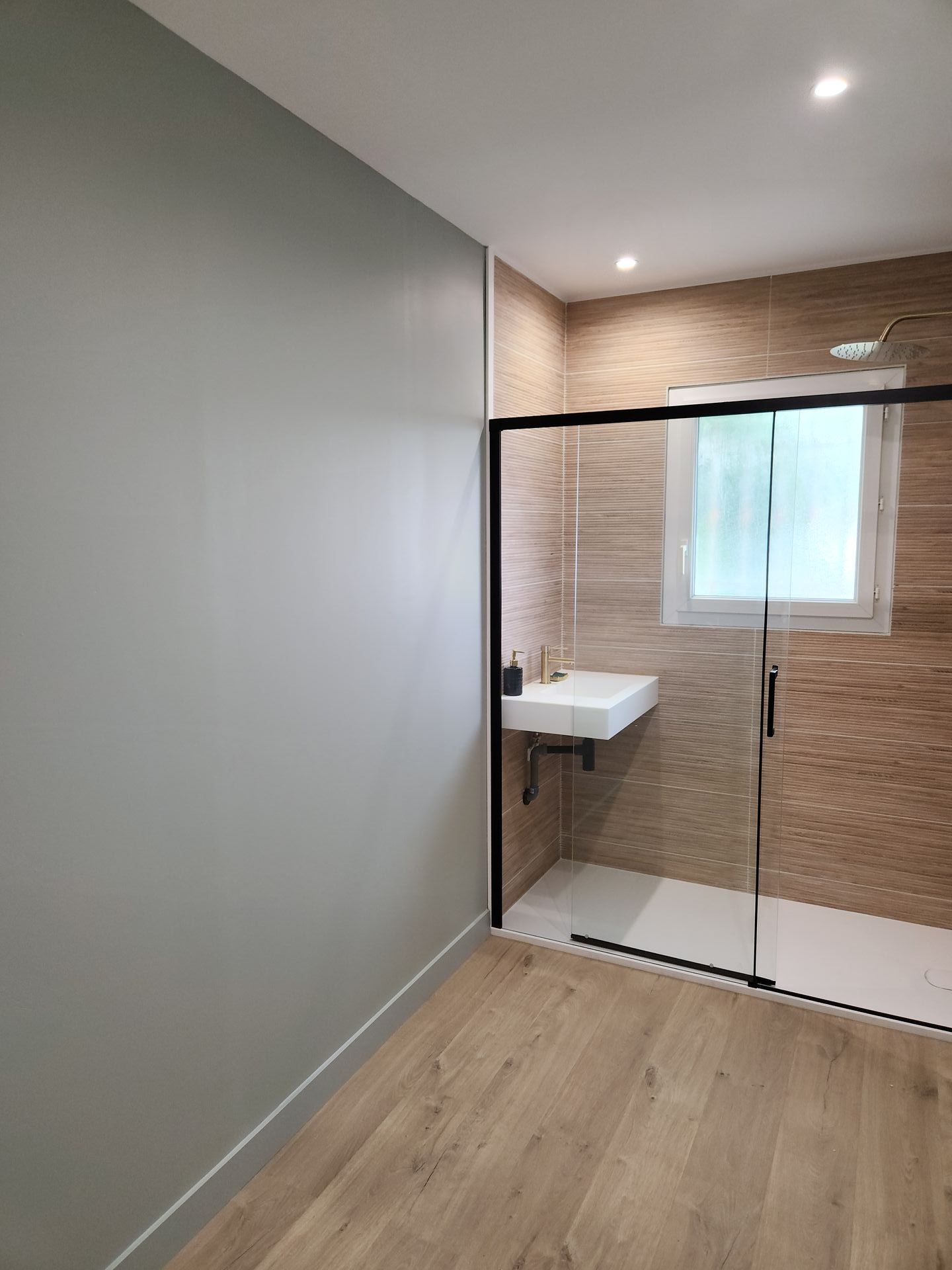 Autre point de vue de la salle de bain avec une partie en bois et le côté mural en couleur taupe.