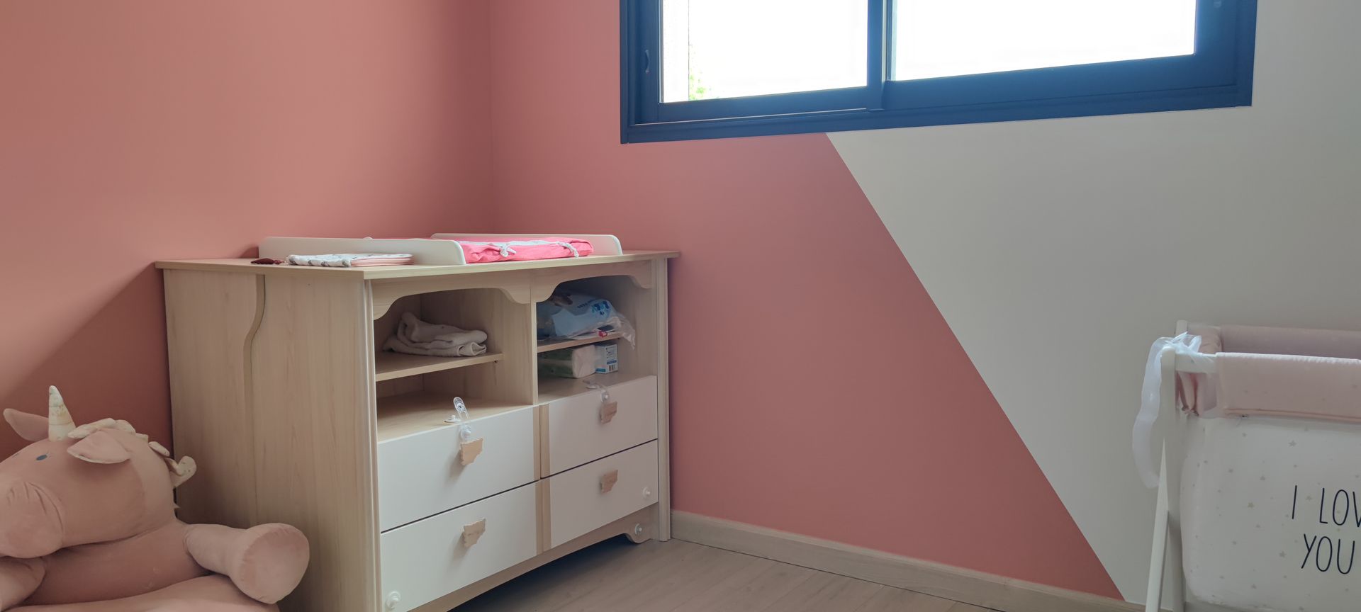 Chambre rose et blanche avec une peluche licorne rose et une table à langer pour bébé.