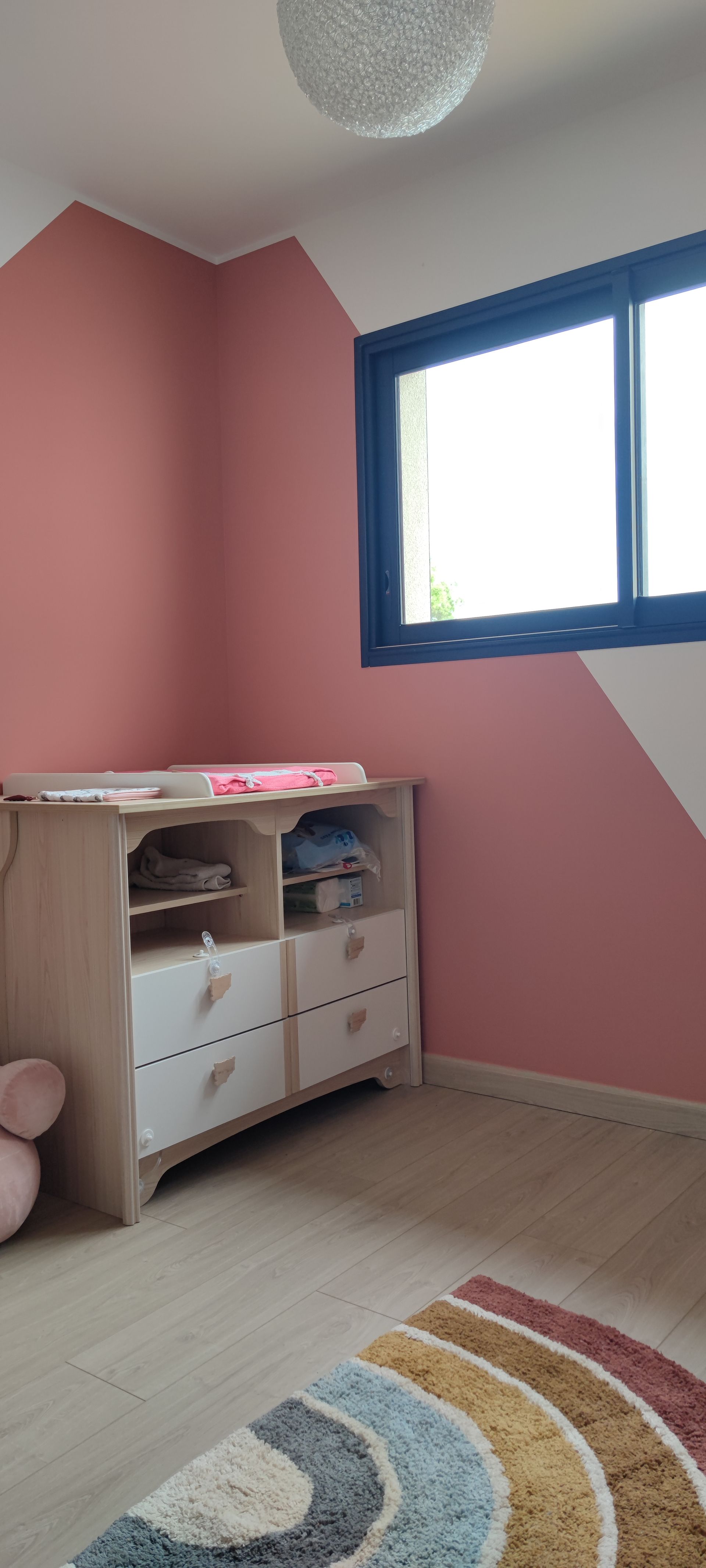 Chambre blanc et rose avec une table à langer et un tapis d'un arc-en-ciel.