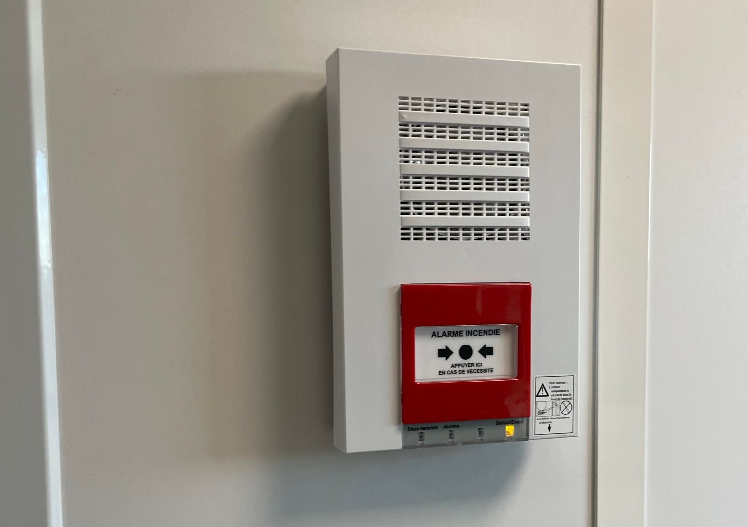 Boîtier d'alarme incendie blanc fixé au mur.